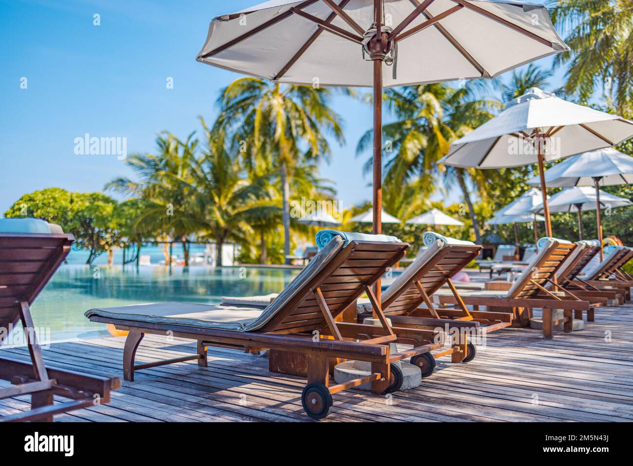 Umbrellas and chairs around outdoor swimming pool in resort hotel for vacation leisure lifestyle. Luxury destination concept, wellbeing lounge Stock Photo