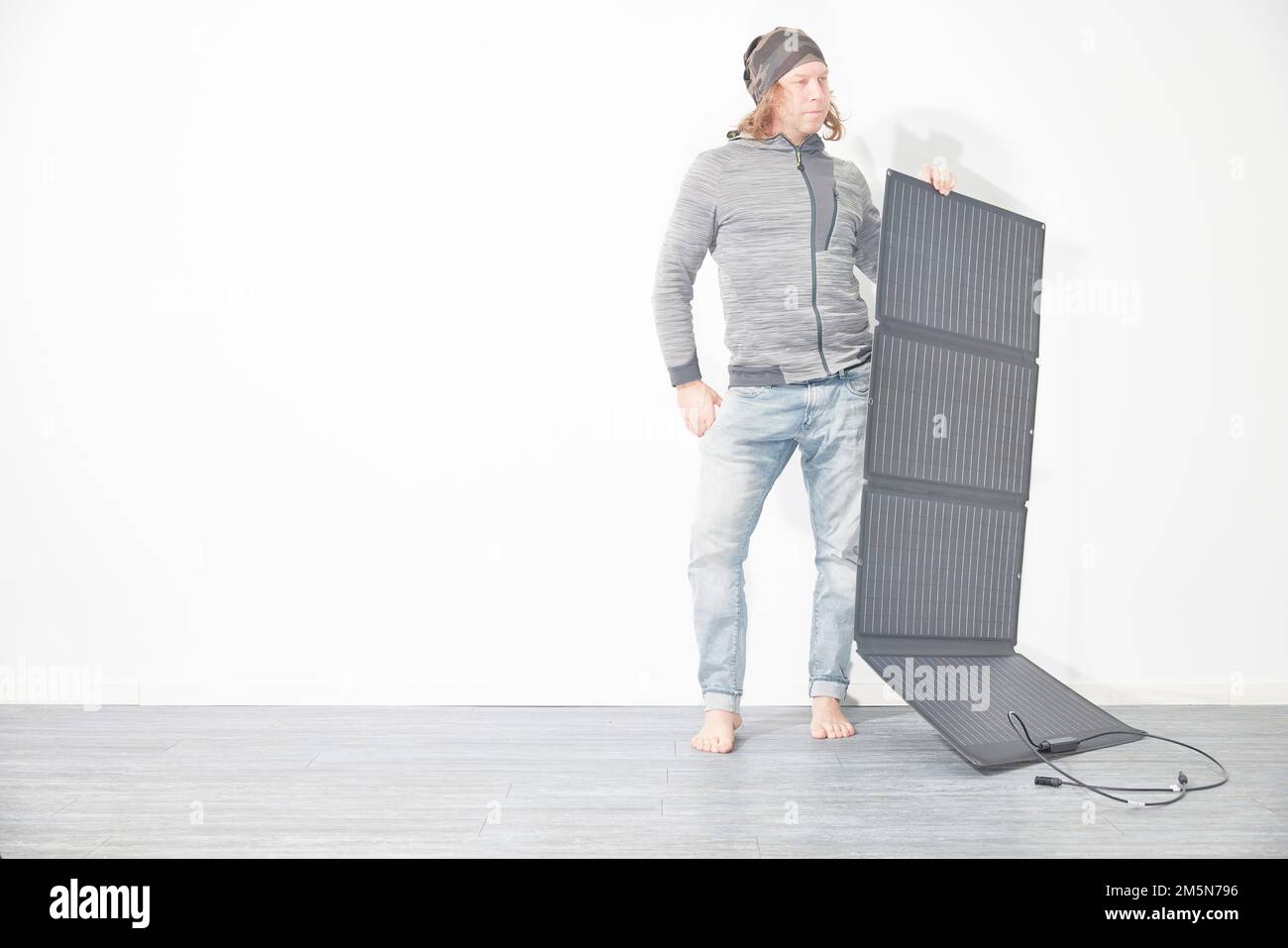 Man with mobile solar panel in front of white wall Stock Photo