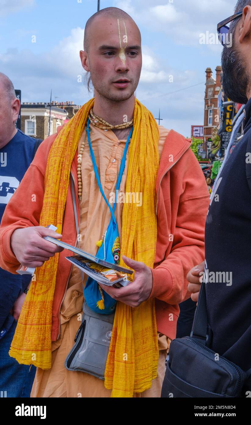 Hare Krishna devotee in saffron coloured robe sells books and talks to people on the streets of Camden Town, London, England Stock Photo