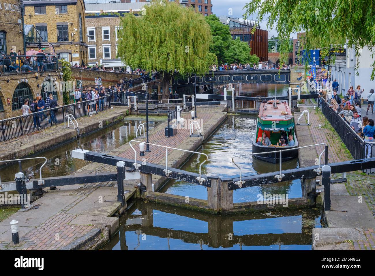 A leisure narrowboat approaches the lock gate at Camden Lock on Regent’s Canal, Camden Town, a popular tourist destination in London, UK. Stock Photo