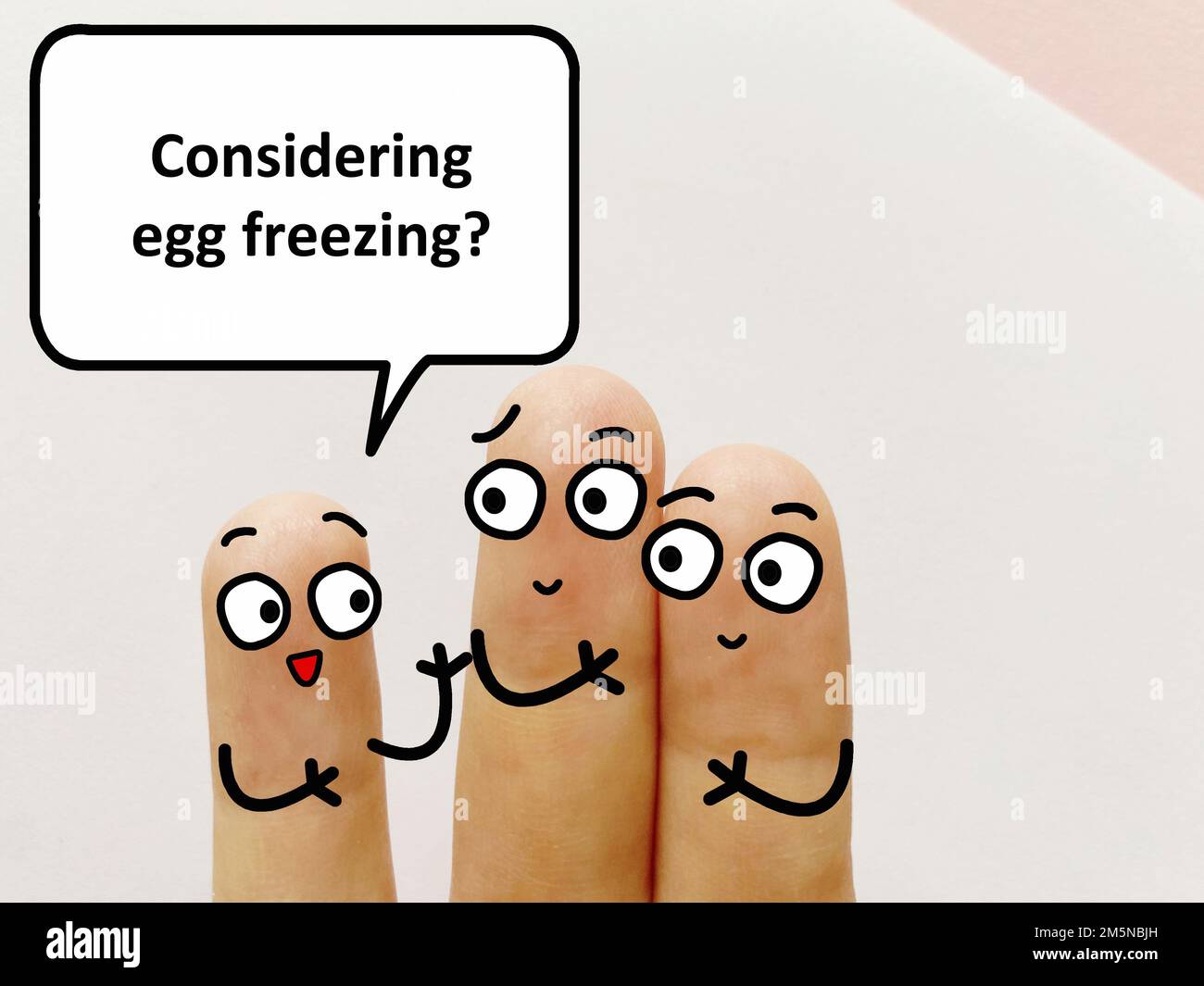 Three fingers are decorated as three person. One of them is asking if they are considering egg freezing. Stock Photo
