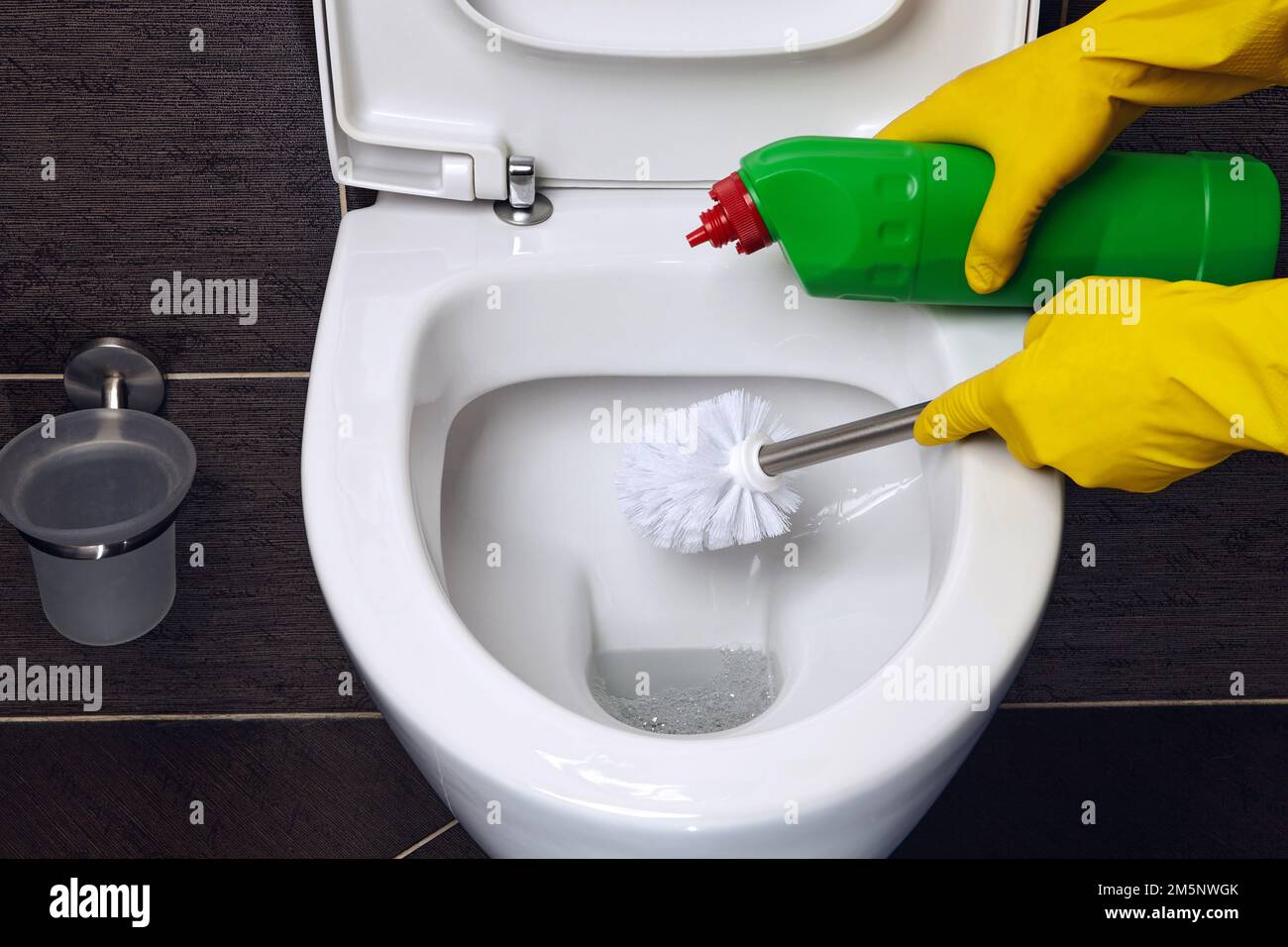 Person in yellow rubber gloves cleans the toilet bowl with a brush and disinfectant Stock Photo