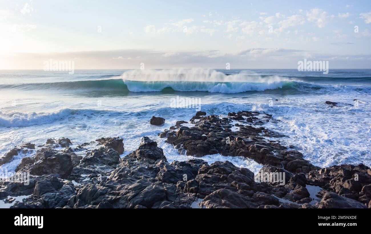 Ocean waves crashing breaking spray front of rocks along beach rocky coastline a morning scenic landscape. Stock Photo