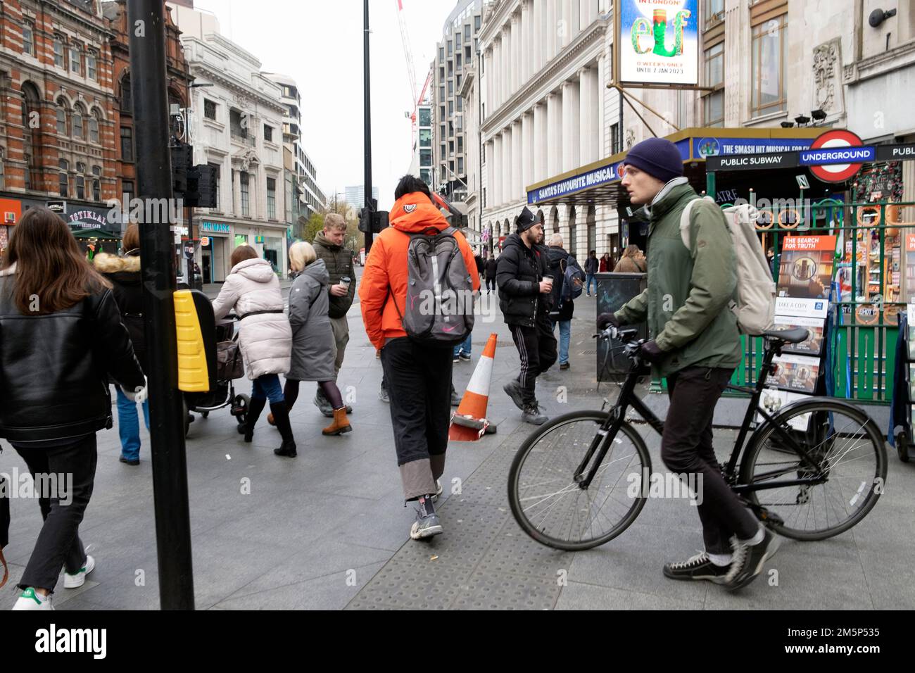 People pedestrians cyclist walking bike on pavement at corner Tottenham Court Road tube station underground sign London UK 2022  KATHY DEWITT Stock Photo