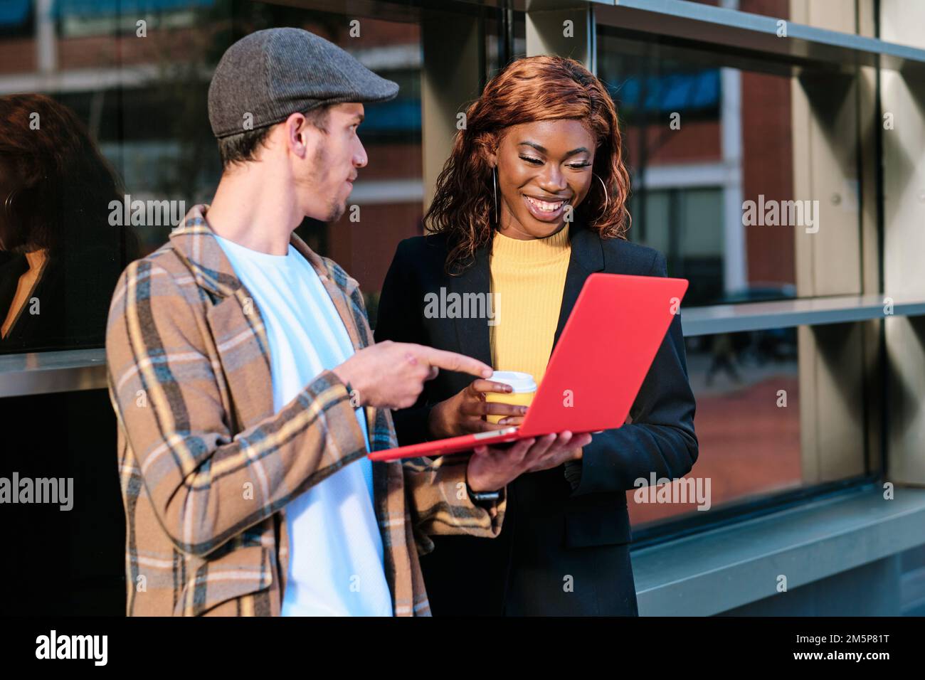 Business colleagues using a laptop while discussing work standing outdoors. Stock Photo