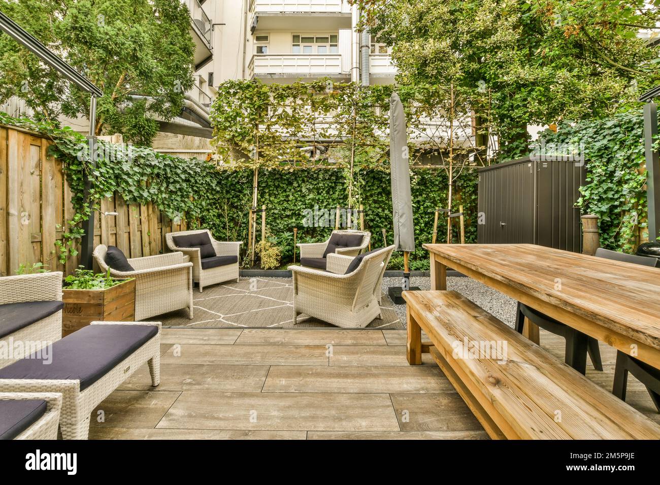 an outdoor patio with wooden furniture and plants on the walls, along with a bench in the middle part of the area Stock Photo