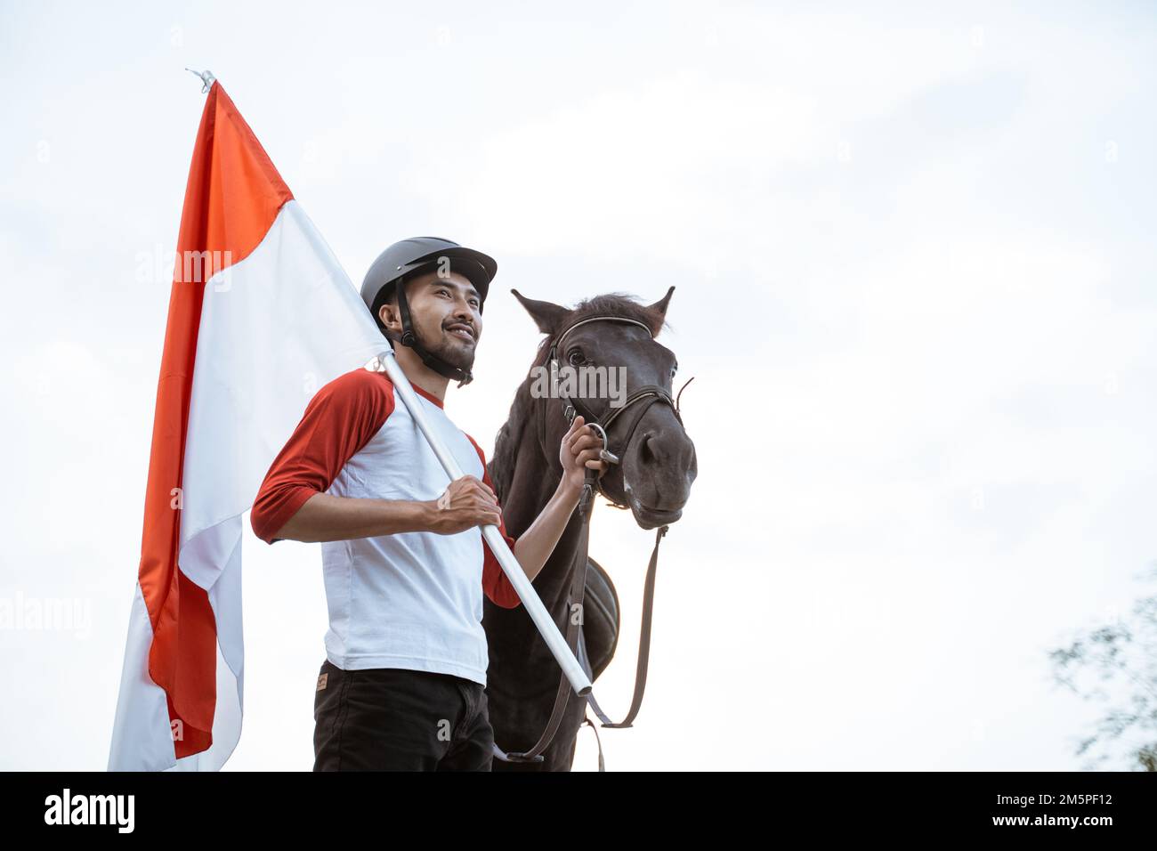 Asian man carrying Indonesian flag holding horse rein beside horse Stock Photo