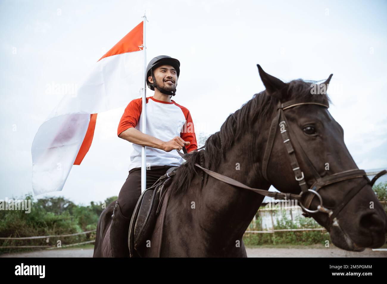 Helmet man riding horse carrying red and white Indonesian flag Stock Photo