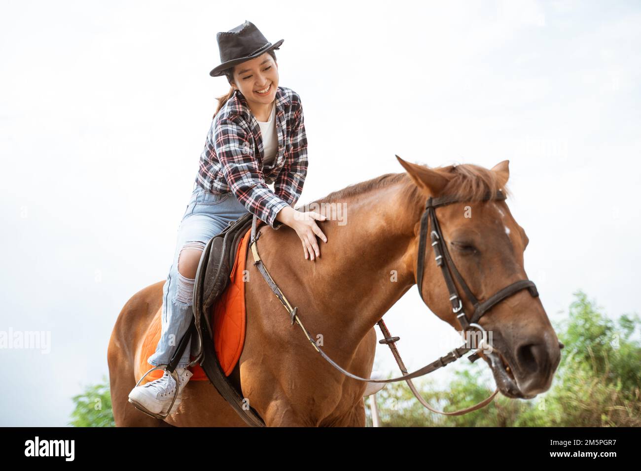 beautiful asian cowboy girl standing beside horse on outdoor background Stock Photo