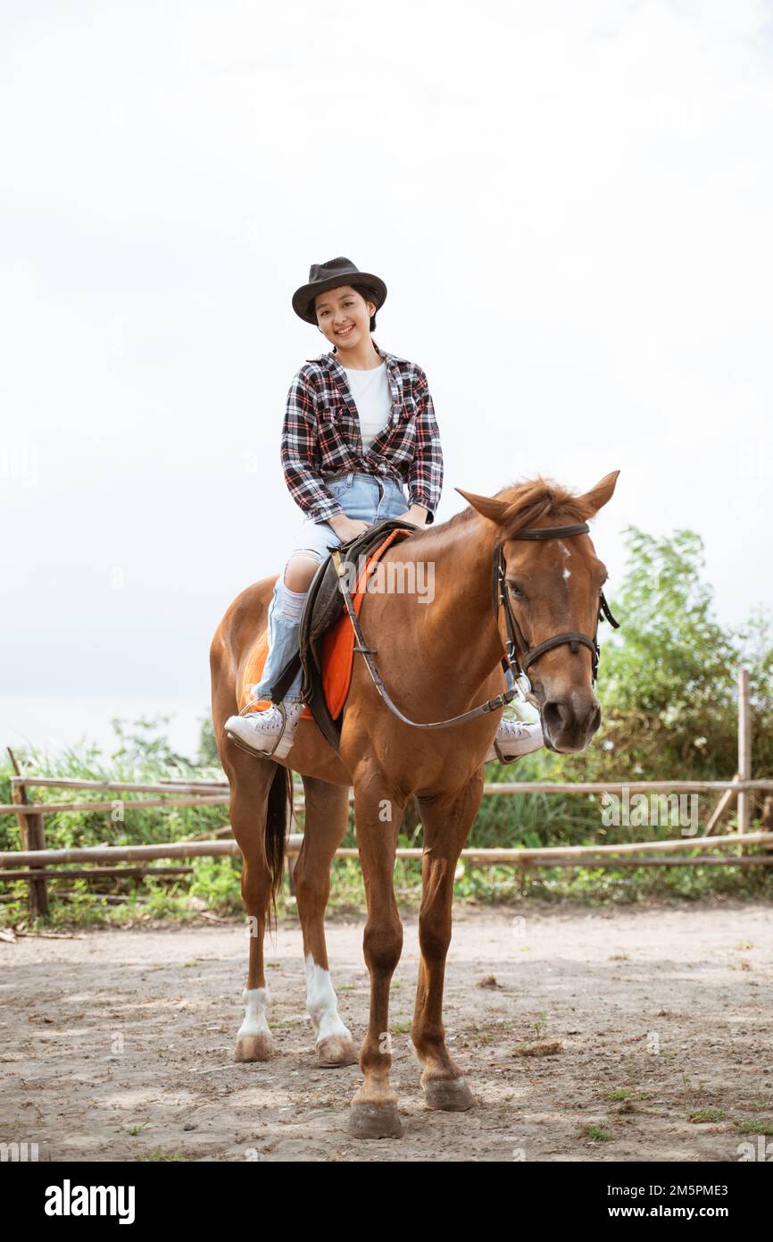 woman in cowboy hat smiling sitting on horse at ranch Stock Photo