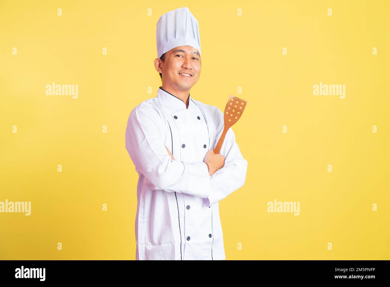 smiling asian male chef holding spatula with hands crossed Stock Photo