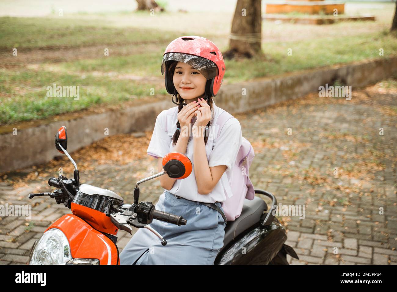 Asian student girl smiling while tightening helmet strap on motorbike Stock Photo