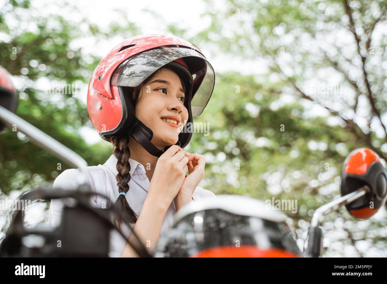 Close up of student girl tightening helmet strap on motorbike Stock Photo