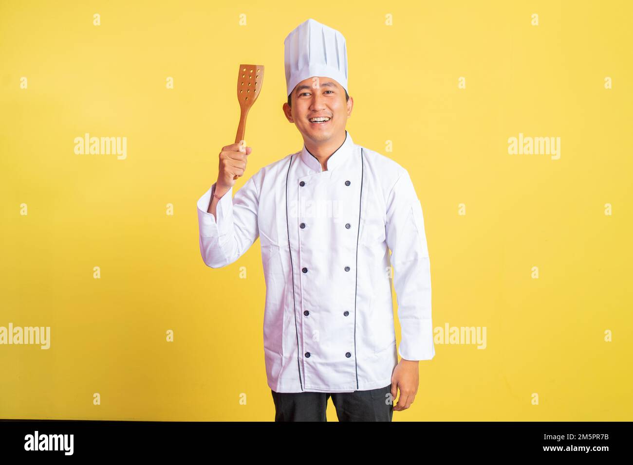 excited male chef wearing a chef jacket holding a spatula Stock Photo