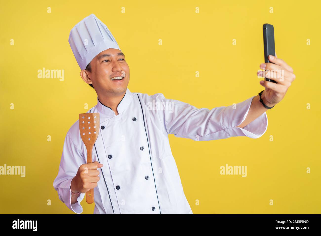 asian male chef wearing chef jacket selfie while holding spatula Stock Photo