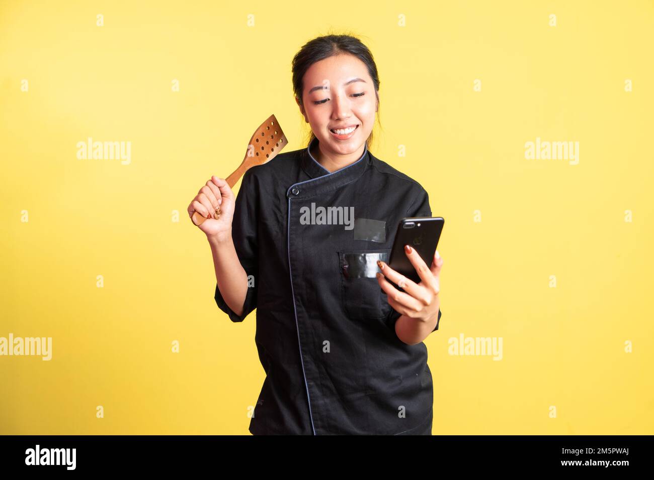 asian female chef using mobile phone and holding spatula Stock Photo