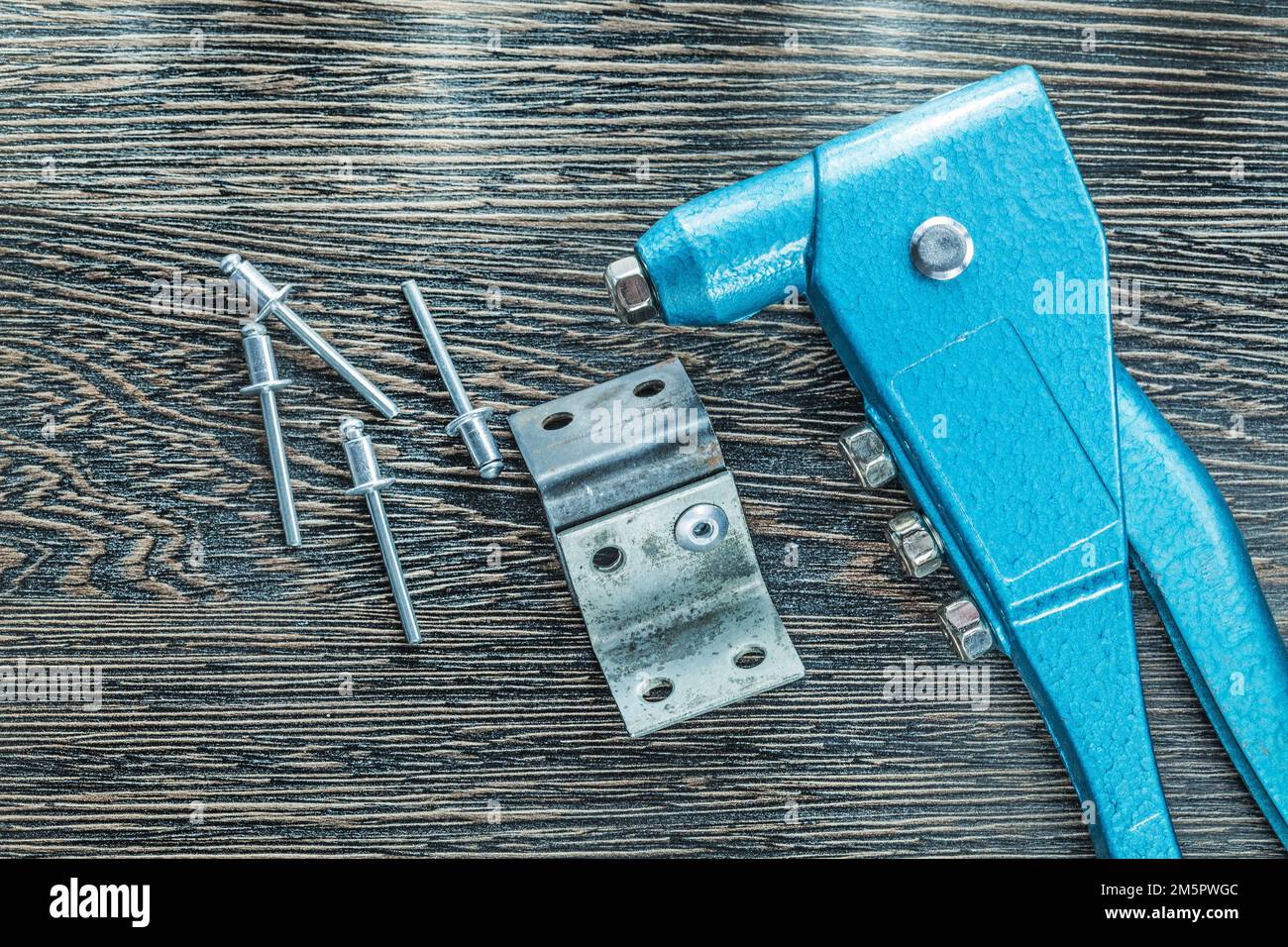 Riveting pliers rivets screws on wooden board. Stock Photo
