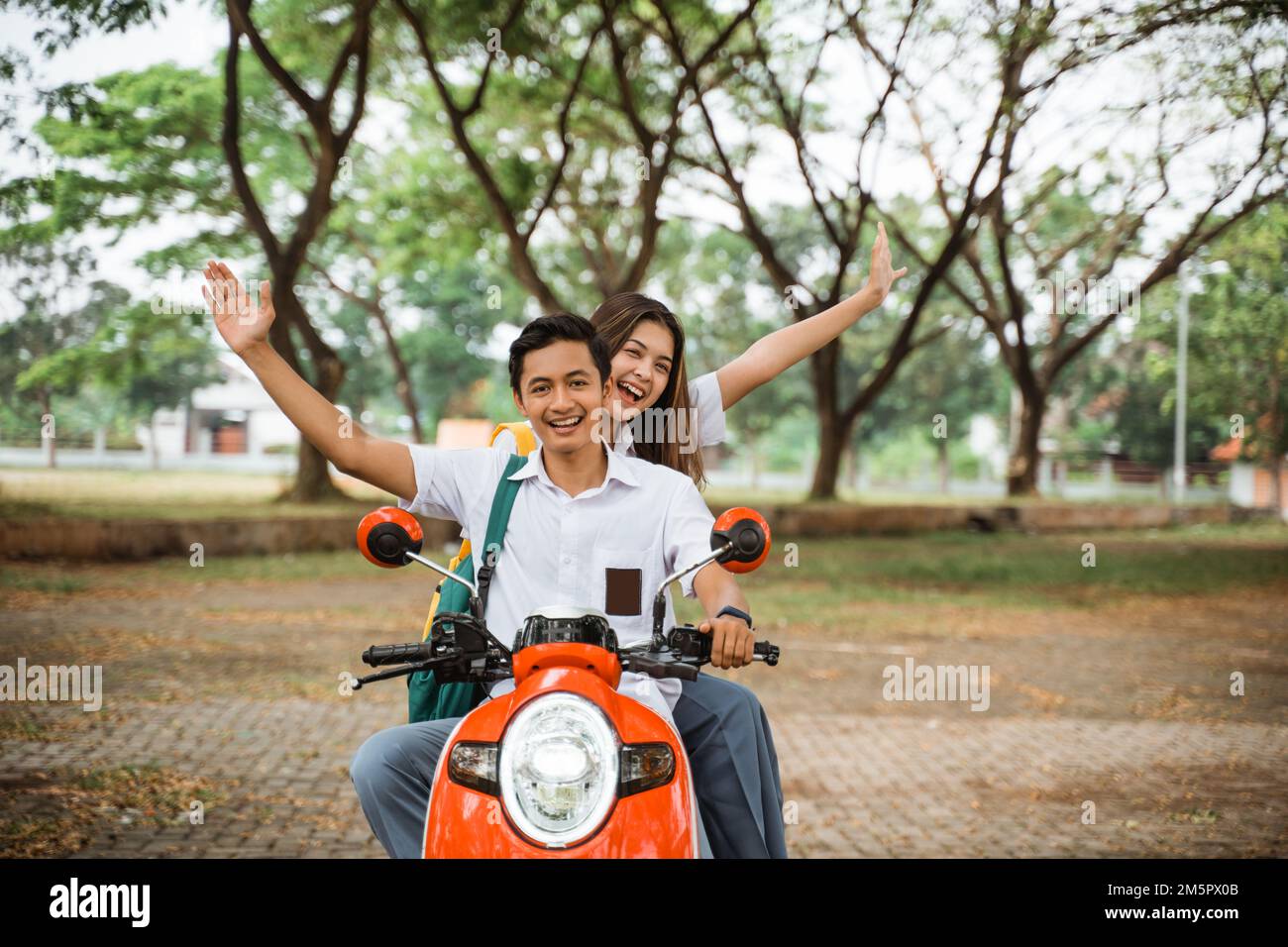 Couple of high school students waving riding motorbike Stock Photo