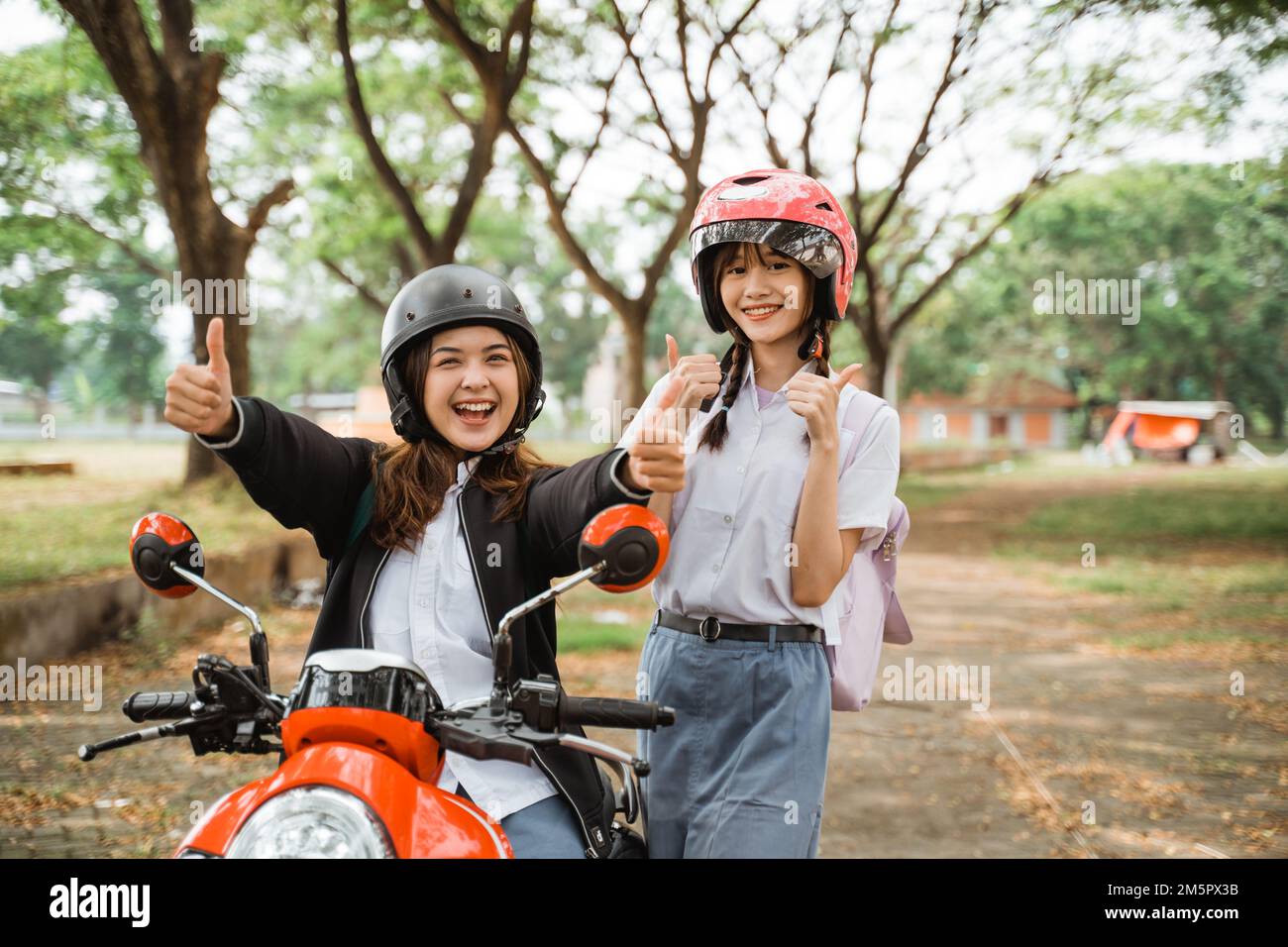 girls with thumbs up going to school on motorbikes Stock Photo