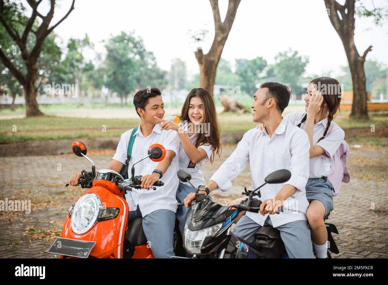Four students joking while riding a motorbike on the road Stock Photo