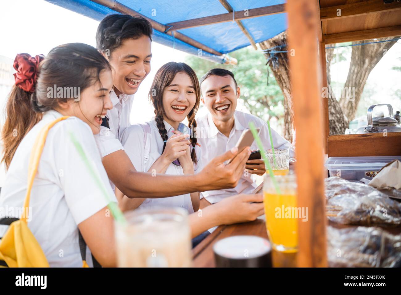 Four high school kids using smartphones together while joking Stock Photo