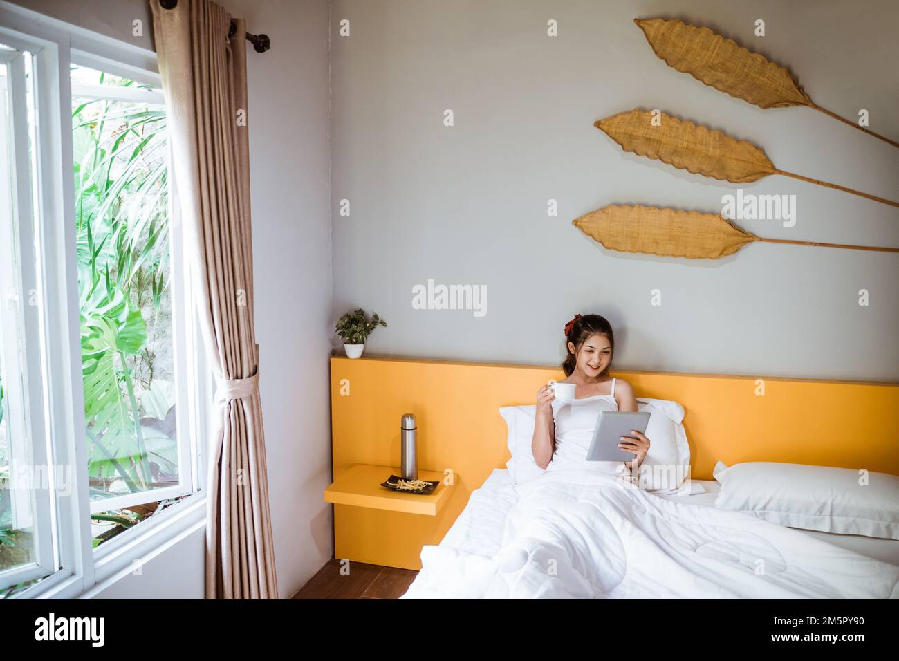 beautiful asian girl on bed waking up using a pad Stock Photo