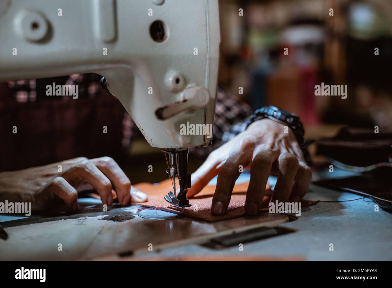 Close up of tailor's hand sewing leather using sewing machine Stock