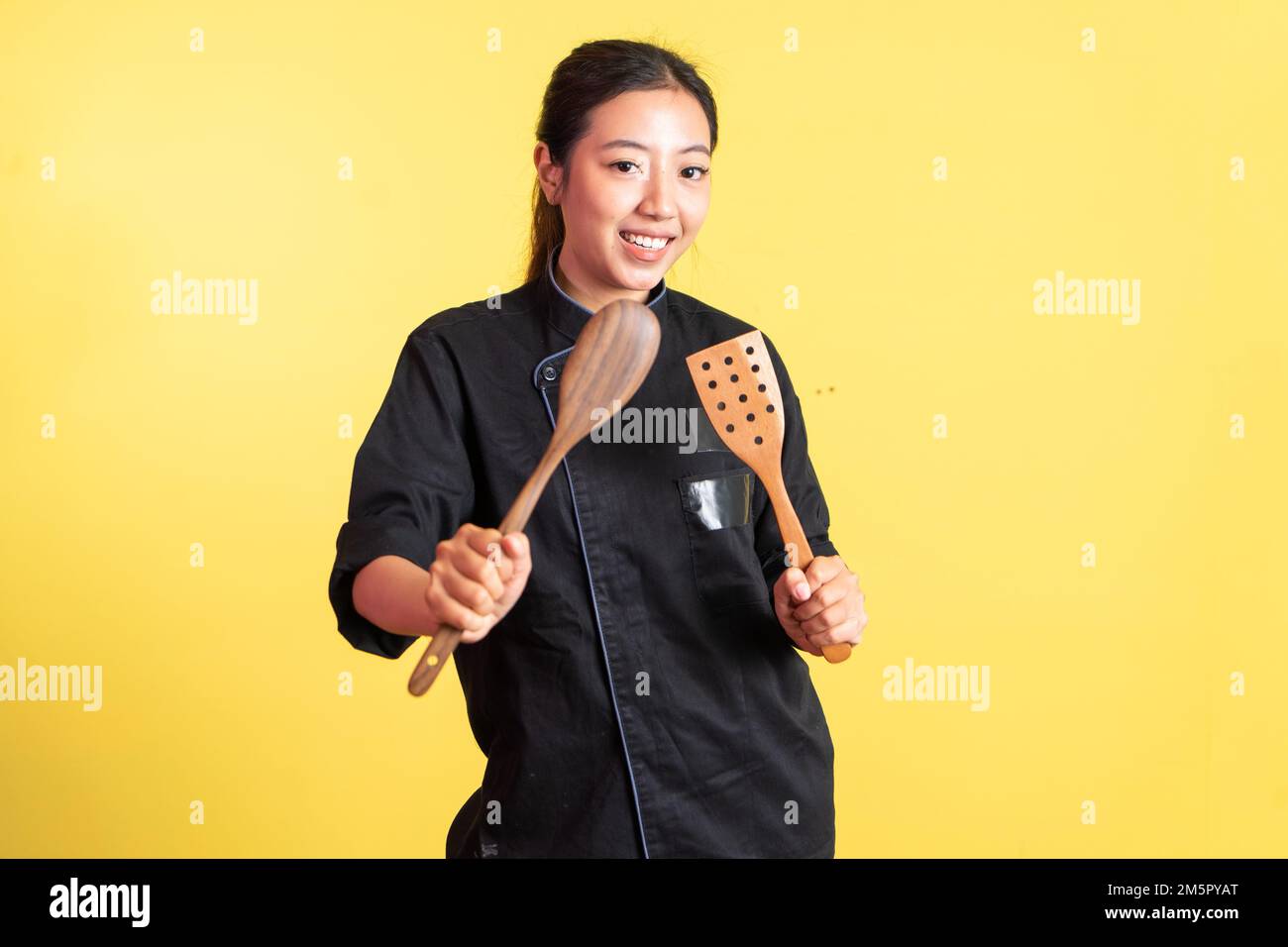 smiling asian female chef holding spatula and spoon Stock Photo