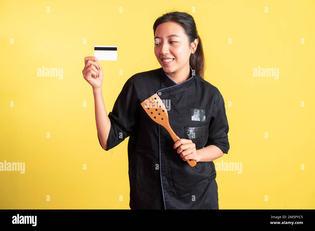 asian female chef showing atm card and holding spatula Stock Photo