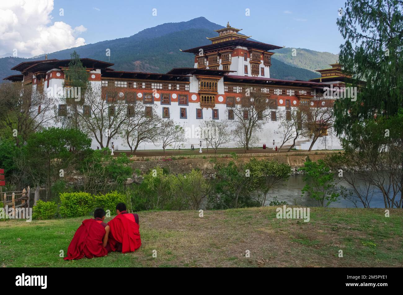Scenic landscape view of Punakha dzong in Western Bhutan, with anonymous buddhist novices sitting on the grass Stock Photo