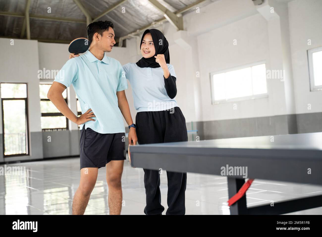 female ping pong athlete in hijab cheers on male partner Stock Photo