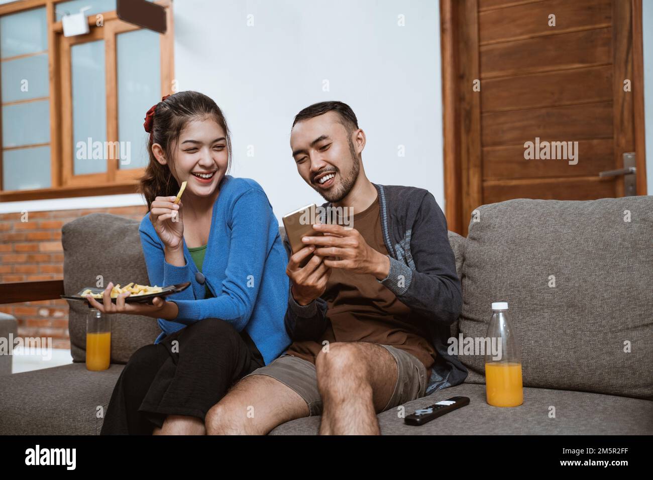 girl laughs as boyfriend shows phone while sitting on sofa Stock Photo