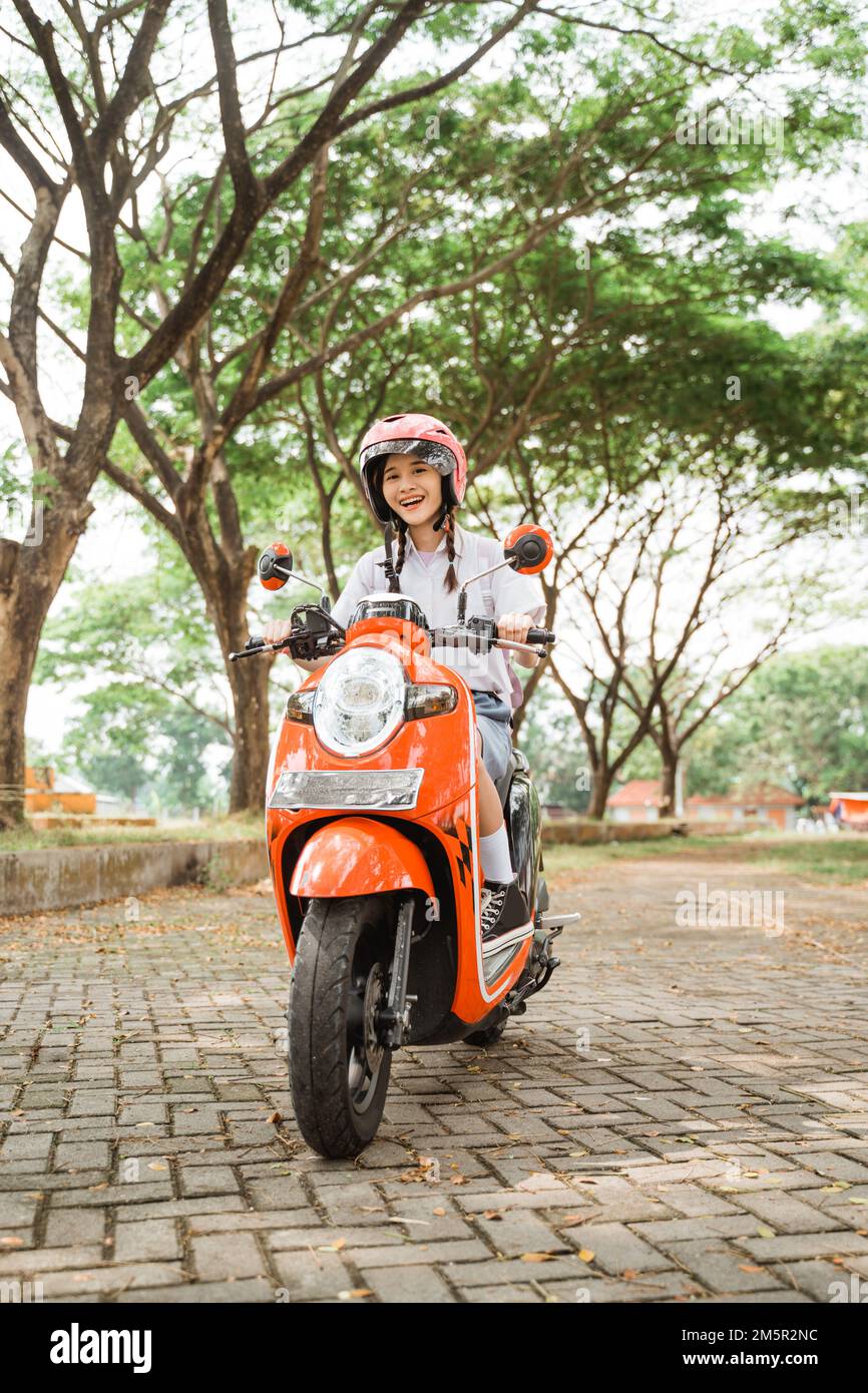 A smiling student girl riding a motorcycle wearing a helmet Stock Photo