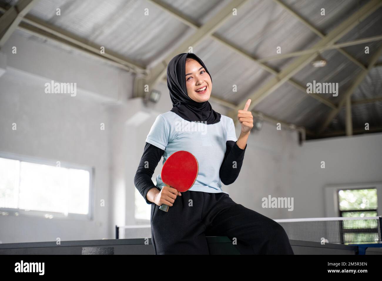 smiling hijabi female athlete holding paddle with thumbs up Stock Photo