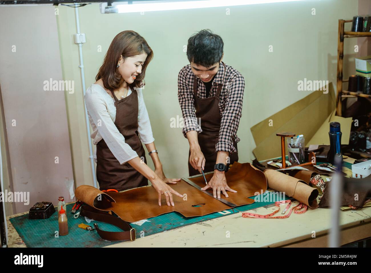 Pair of asian tailors measuring while patterning leather at work Stock Photo