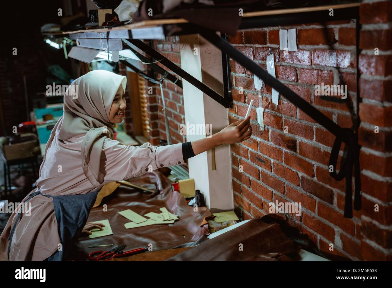 Craftswoman in veil makes sticky notes on wall while working Stock Photo