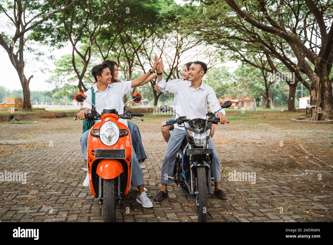 Students clapping their hands with their friends while riding motorbike Stock Photo