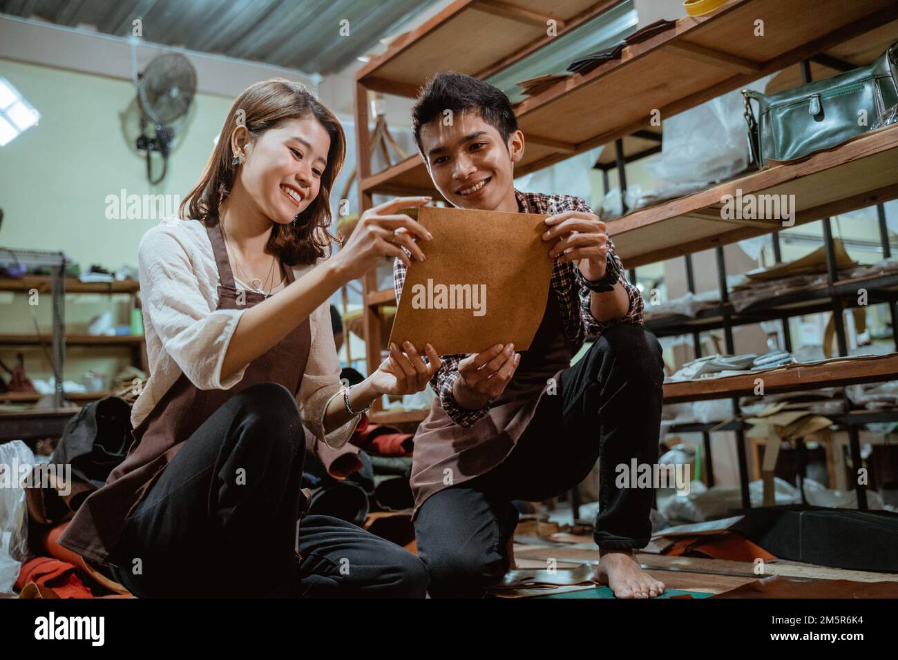 Asian craftswoman and a craftsman holding and observing leather Stock ...