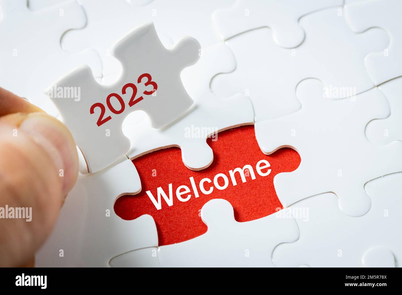 Rok 2023, witamy,  Biały Puzzle z rokiem trzymany w palcach, napis na czerwonym tle, Powitanie nowego roku, Oczekiwanie pozytywne zmiany Stock Photo