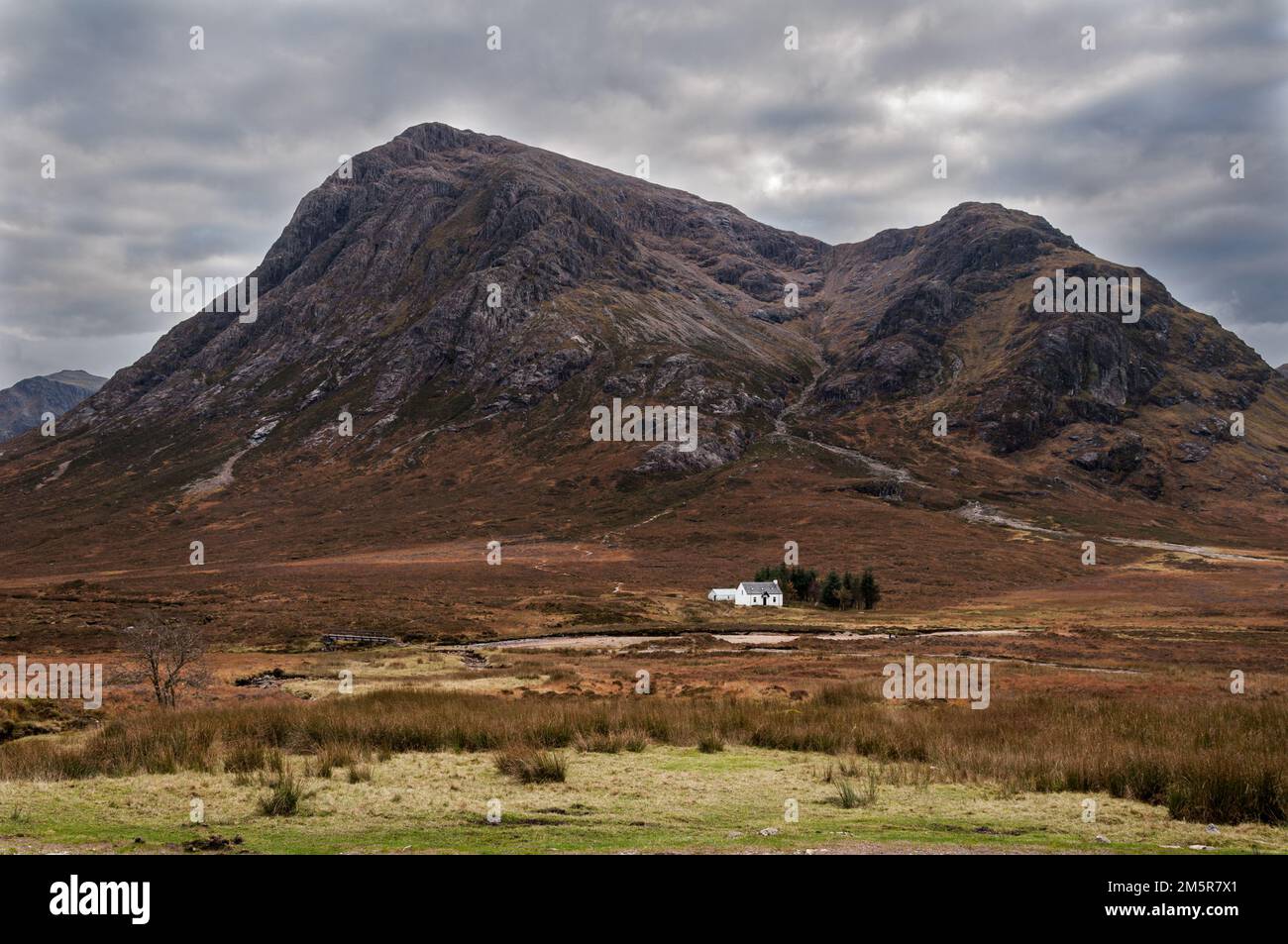 Buachaille Etive Mòr under a leaden sky at the entrance to Glencoe with the iconic whitewashed cottage at its base Stock Photo