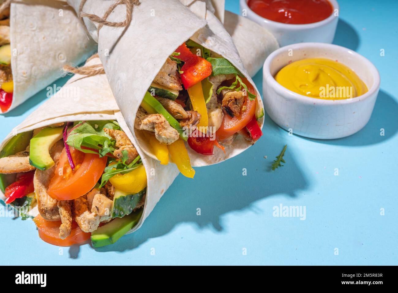 Classic street food shawarma or burrito, healthy sandwich wrapped in tortilla flat bread with fried chicken meat, fresh vegetables, sauce, on bright b Stock Photo