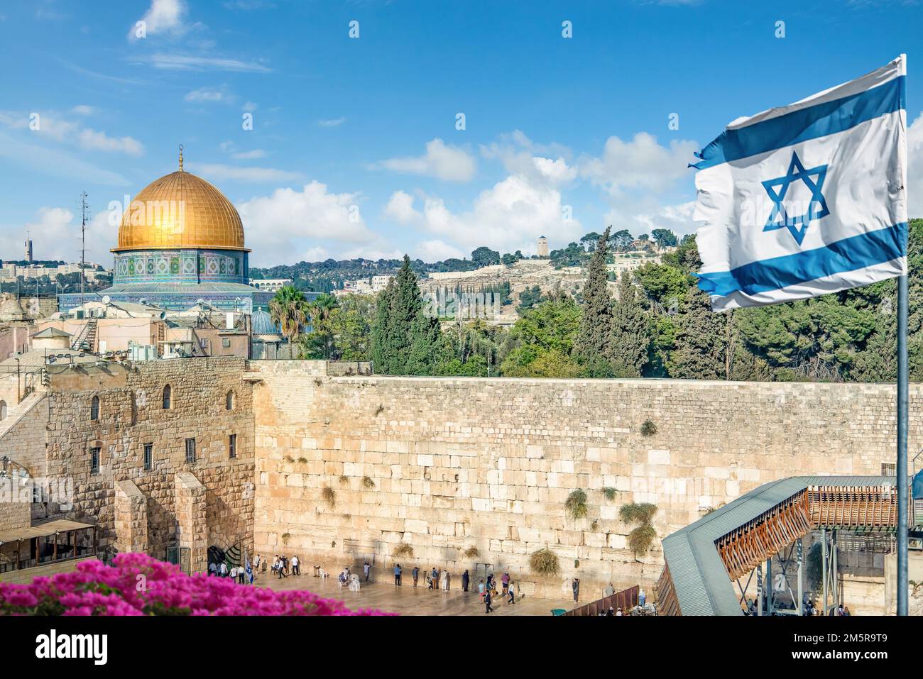 An Israeli flag blows as jewish orthodox believers read the Torah and pray facing the Western Wall also known as Wailing Wall in Old City in Jerusalem Stock Photo