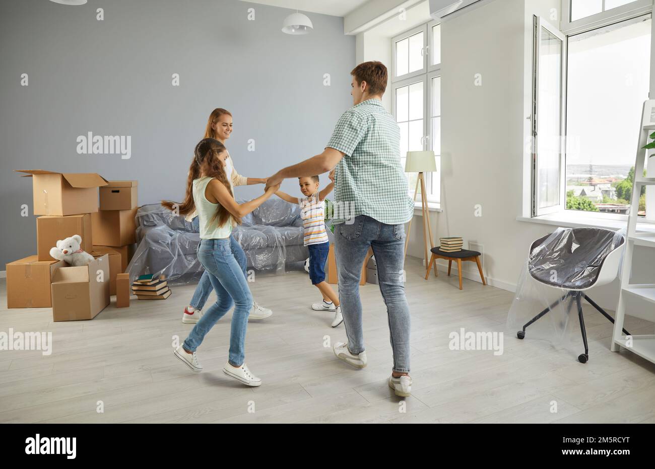 Cheerful young family with children dancing and having fun while moving to new apartment. Stock Photo
