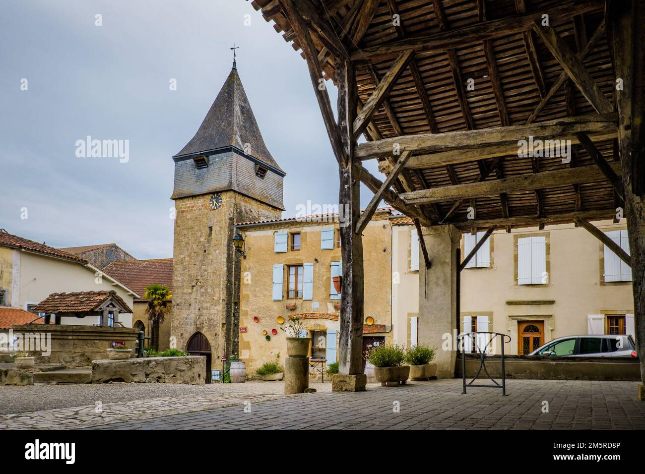 The main square, the wooden market hall and the church clock tower of the medieval village of Bassoues in the south of France (Gers) Stock Photo