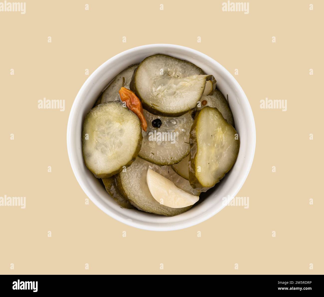 Pickled sliced cucumbers in brine in a bowl on yellow background