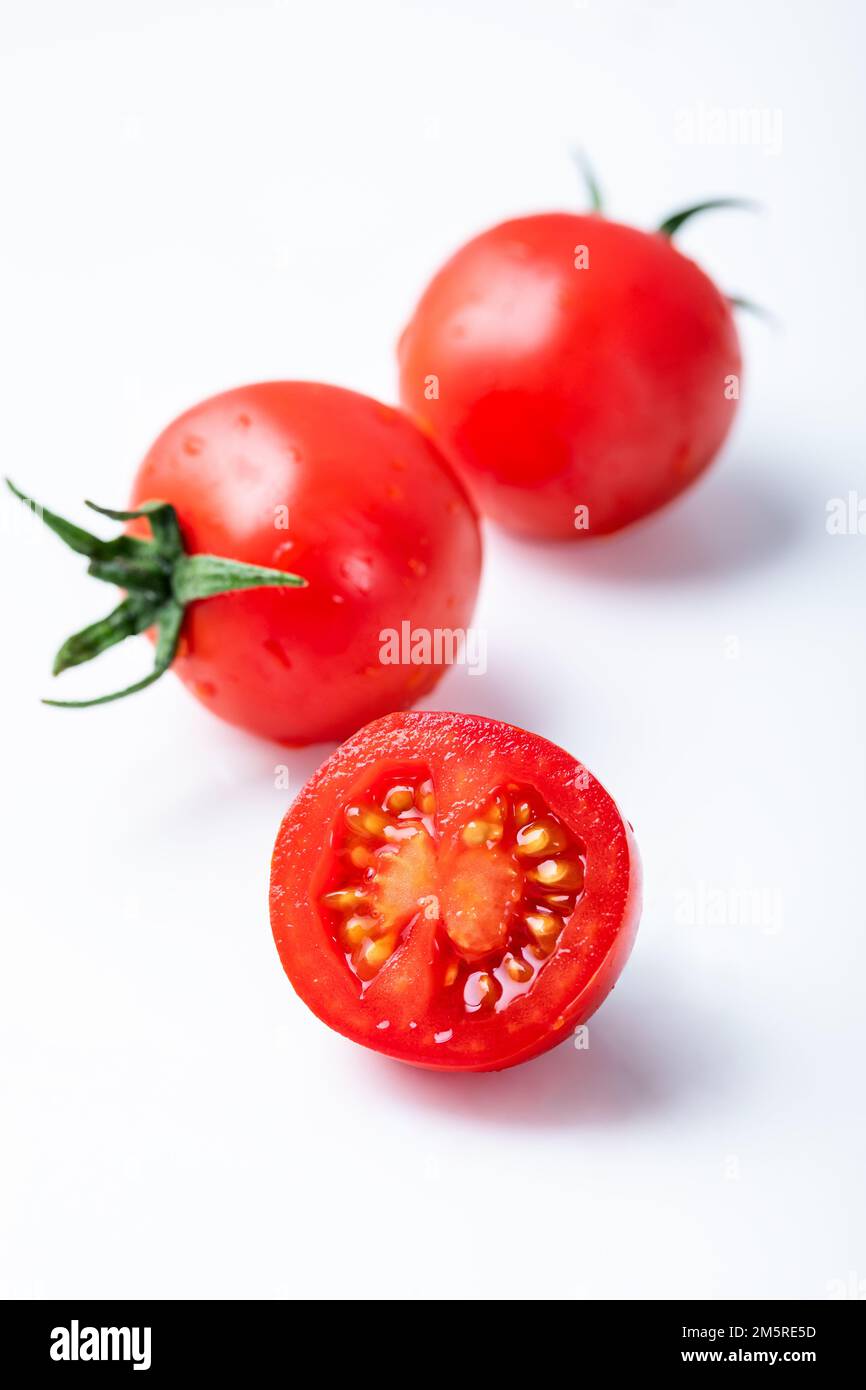 Two whole and cut wedge of fresh, red tomato isolated on white background. Cherry tomatoes on white background. Stock Photo