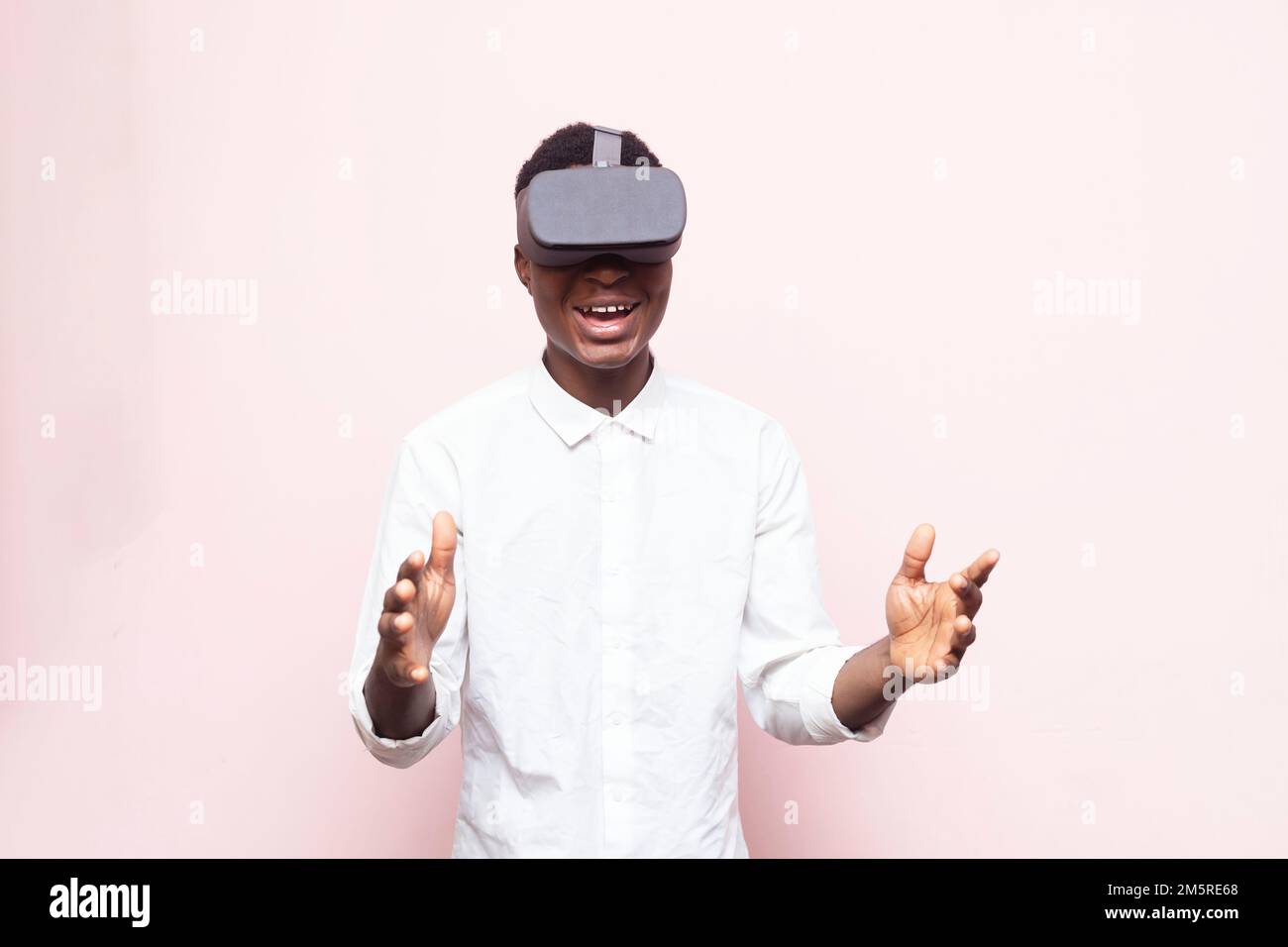 An excited  African gamer wearing VR googles, simulated 3D environment isolated on pink background Stock Photo
