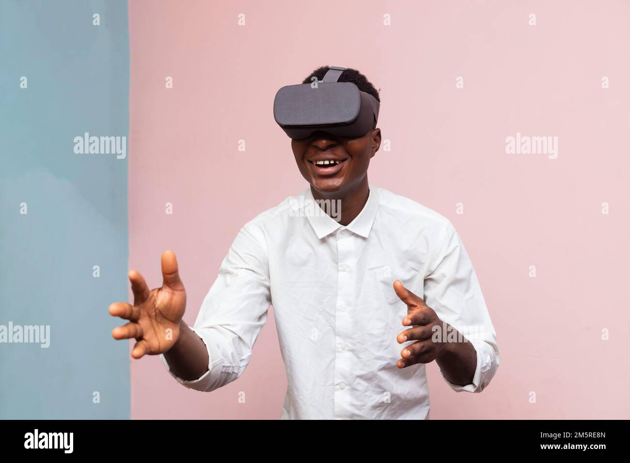An excited  African gamer wearing VR googles, simulated 3D environment isolated on pink background Stock Photo