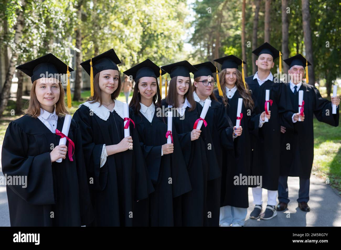 Row of young people in graduation gowns outdoors. Age student. Stock Photo