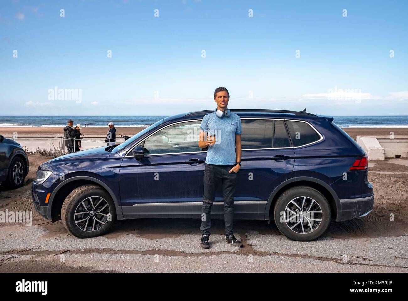 Portrait of mid adult man with coffee standing by blue car at beach Stock Photo